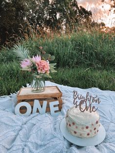 a cake sitting on top of a blanket next to a wooden sign that says one