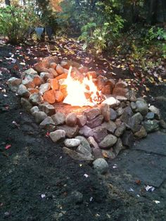 a fire pit made out of rocks in the middle of a forest with leaves on the ground