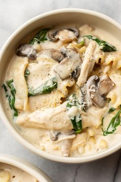 two bowls filled with pasta and mushrooms on top of a marble countertop next to another bowl