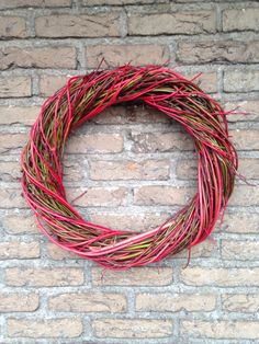 a close up of a wreath on a brick wall with grass in the middle and red yarn around it