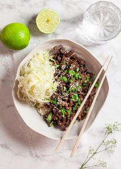 a white plate topped with meat and rice next to chopsticks