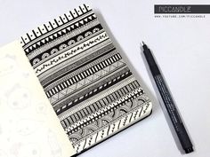 a notebook with black and white designs on it next to a marker, pen and paper