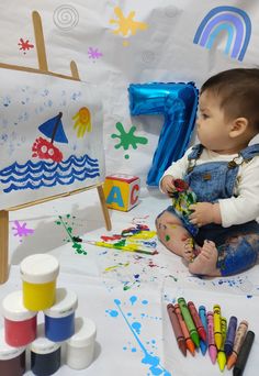 a baby sitting on the ground with crayons and paint