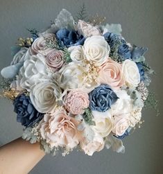 a bridal bouquet is being held by someone's hand in front of a gray wall