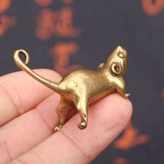 a small gold colored cat brooch sitting on someone's hand with chinese characters in the background