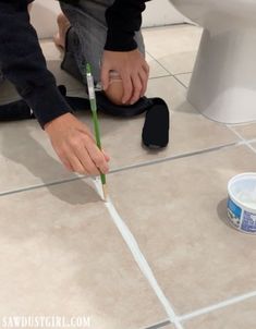 a person using a toothbrush to clean a bathroom floor with a toilet in the background