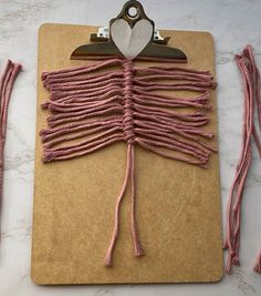 a clipboard with some pink string attached to it and a heart shaped object on top