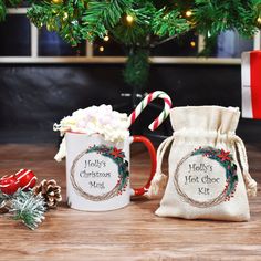 two coffee mugs with candy canes and holly's hot chocolate kit in front of a christmas tree