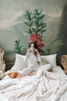 a woman sitting on top of a bed holding a cup in front of her face