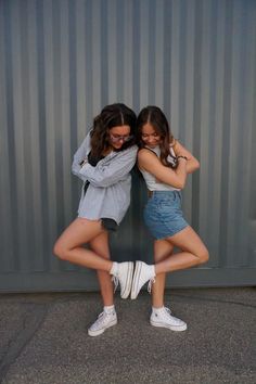 two young women are hugging each other in front of a metal wall with their arms around one another