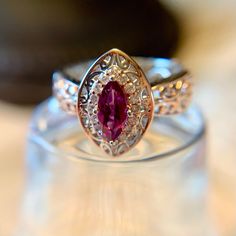 a close up of a ring with a red stone in the center and white diamonds around it