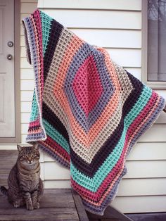 a cat sitting next to a crocheted blanket on top of a wooden porch