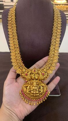 a hand holding a gold necklace with red beads