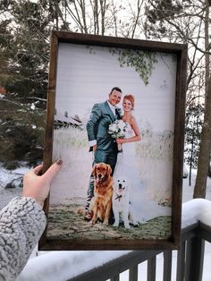 a person holding up a photo with two dogs in front of them and snow on the ground