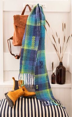 a blue and green plaid blanket sitting on top of a bench next to a purse