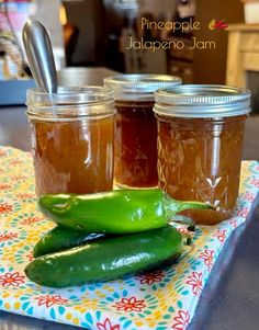 three jars filled with pickles sitting on top of a table next to spoons