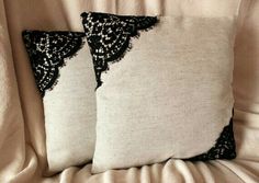 two pillows with black lace on them sitting on a bed