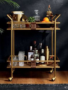 a bar cart with bottles and glasses on it in front of a potted plant