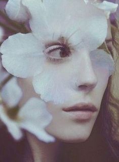 a woman with white flowers in her hair and eye make - up is looking at the camera