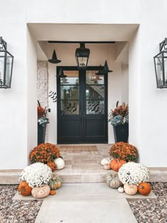 the front entrance to a home with pumpkins and flowers