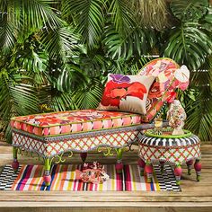 an upholstered chaise lounge in front of palm trees and rugs on a wooden deck