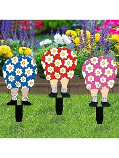 three lawn decorations in the shape of people with flowers on their backs, standing in front of