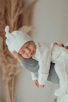 a newborn baby is being held up by someone's hand while wearing a white knitted hat