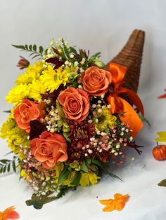 a bouquet of orange and yellow flowers on a white tablecloth with autumn leaves around it