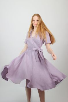 a woman in a purple dress poses for the camera with her hands behind her back