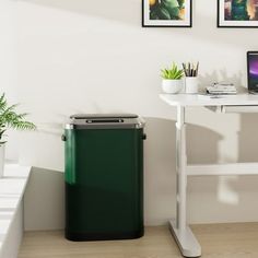 a laptop computer sitting on top of a white desk next to a trash can and plant