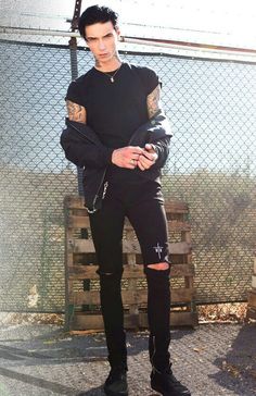 a man in black clothes standing next to a fence