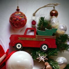 a red toy truck sitting on top of a christmas tree next to ornaments and baubles