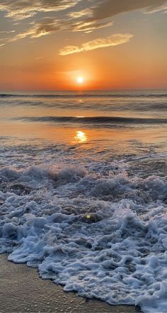 the sun is setting over the ocean with waves crashing on the shore and in the foreground