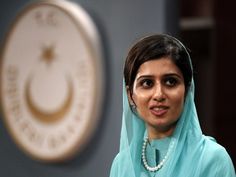 a woman wearing a blue hijab standing in front of the logo of the cia