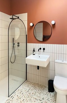 a white toilet sitting next to a walk in shower under a bathroom mirror and sink