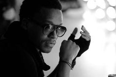 a man wearing glasses sitting at a table with his hand up to the camera and pointing