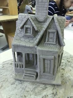 a clay house sitting on top of a counter next to a person working on a project