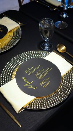 a table set with black and gold place settings, silverware, and napkins