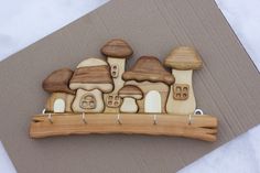 a wooden brooch with mushrooms and houses on it sitting on a piece of cardboard