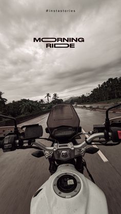 the front end of a motorcycle driving down a road with palm trees in the background