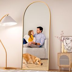 a man and woman sitting on a couch in front of a mirror with a dog laying next to them