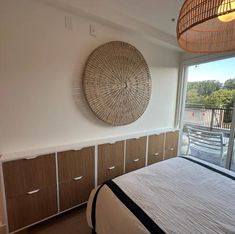 a bed sitting next to a window in a bedroom under a light fixture with a wicker basket hanging on the wall