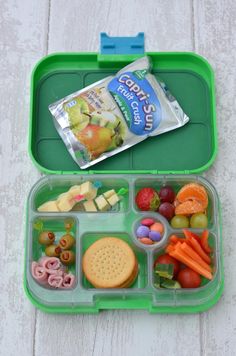 a green lunch box filled with fruits and vegetables next to a bag of crackers