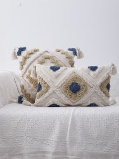 two decorative pillows sitting on top of a white couch next to a pillow with blue accents