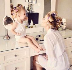 a woman sitting on top of a white stool in front of a mirror brushing her hair