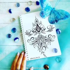 a woman's hand holding a blue butterfly next to a spiral notebook with an intricate design on it