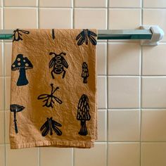 a tea towel hanging on a rack in front of a tiled wall with bugs and mushrooms