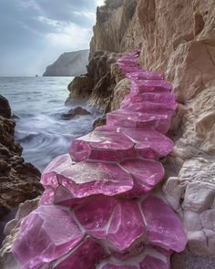 purple rocks are lined up along the edge of a cliff by the ocean with waves coming in