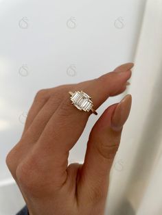 a woman's hand holding an engagement ring with two baguettes on it