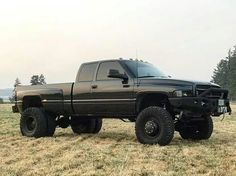 a large black truck parked on top of a dry grass covered field with trees in the background